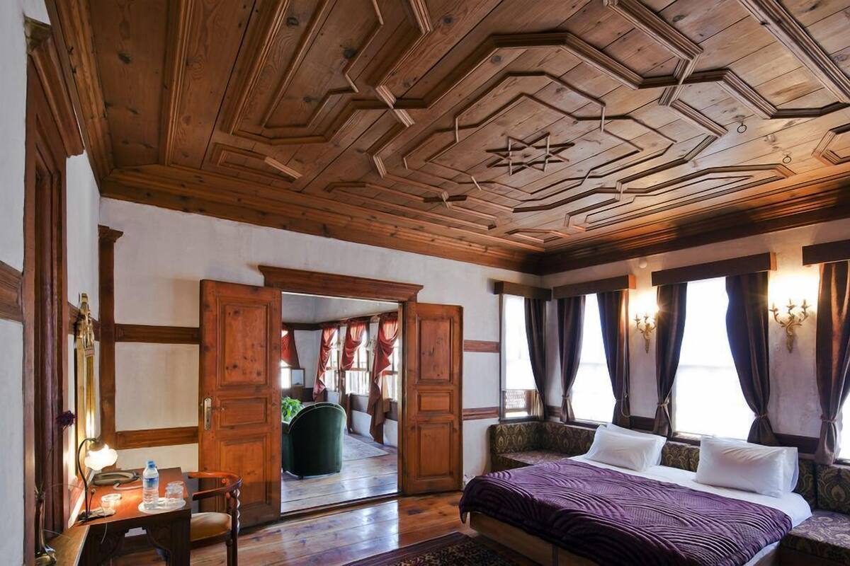 Una habitación con techo de madera, una cama, un escritorio con silla y una ventana con cortinas.