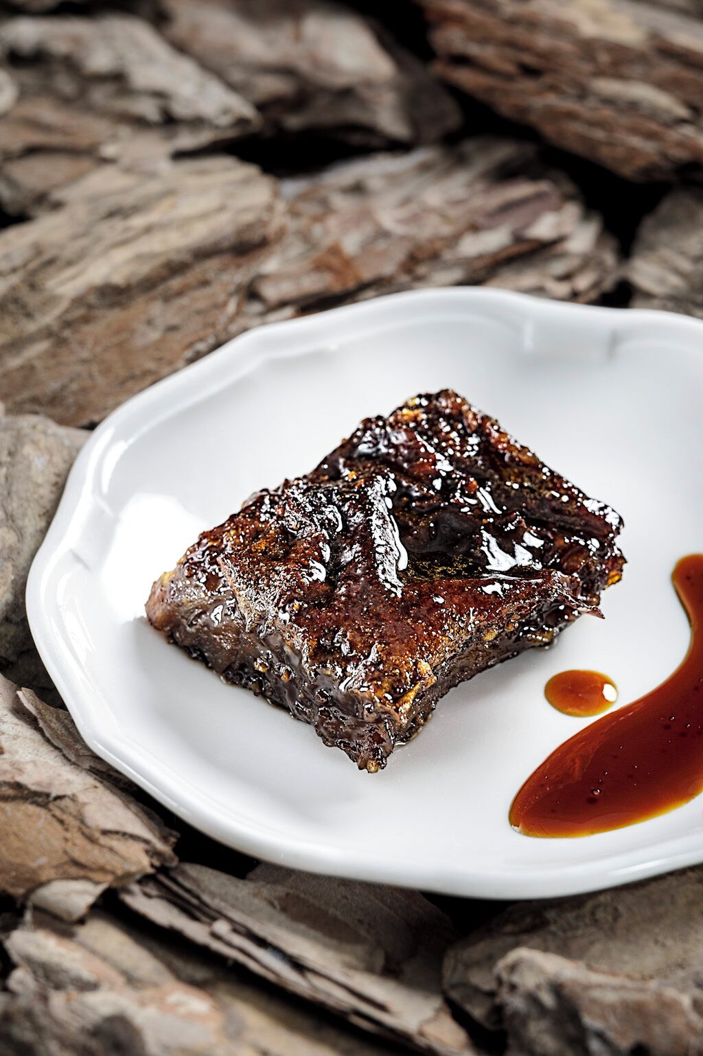 A piece of meat on a white plate with a dark sauce.