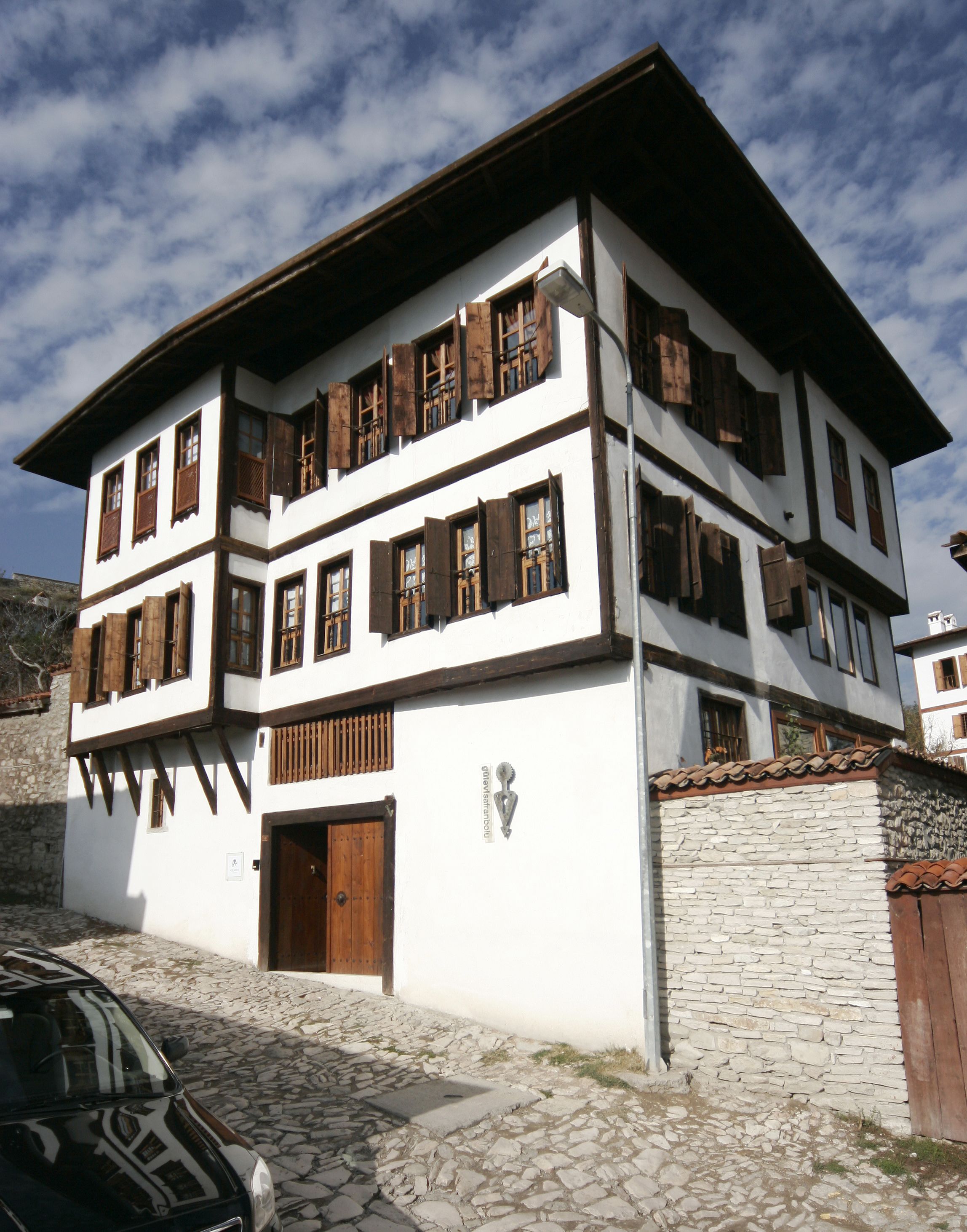 Un edificio de dos pisos con fachada blanca, contraventanas de madera y una pared de piedra.