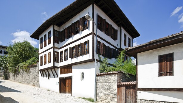 Ein traditionelles, zweistöckiges Gebäude mit steinernem Sockel und Holzkonstruktion, das mehrere Fenster mit Holzhörnern aufweist.