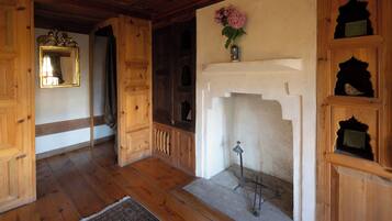 Une pièce au plancher de bois, dotée d’une cheminée, d’un miroir et d’étagères ornées d’objets décoratifs.