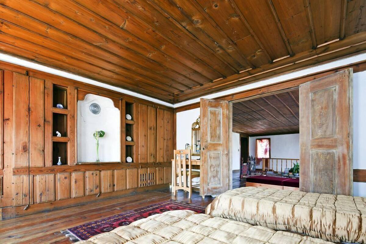 Una habitación rústica con paredes de madera, una cama, una silla y una mesa con mantel rojo.
