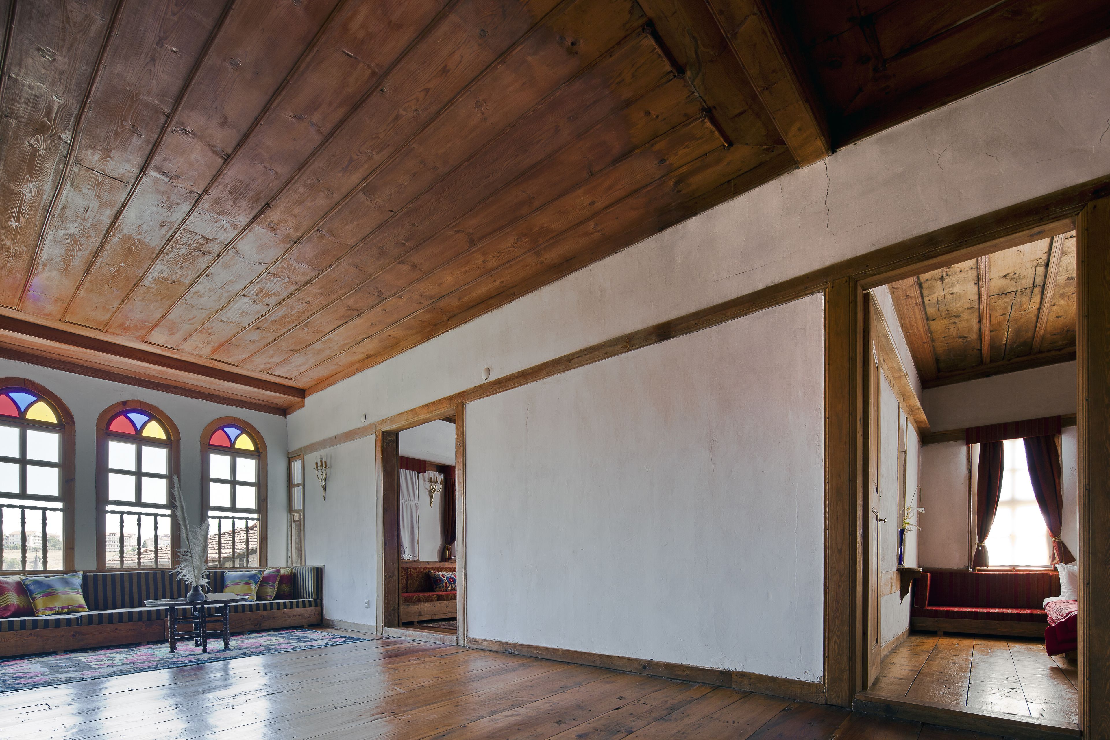 A spacious room with wooden beams on the ceiling, a large window with stained glass, and a bench along the wall.