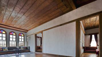 A spacious room with wooden beams on the ceiling, a large window with stained glass, and a bench along the wall.