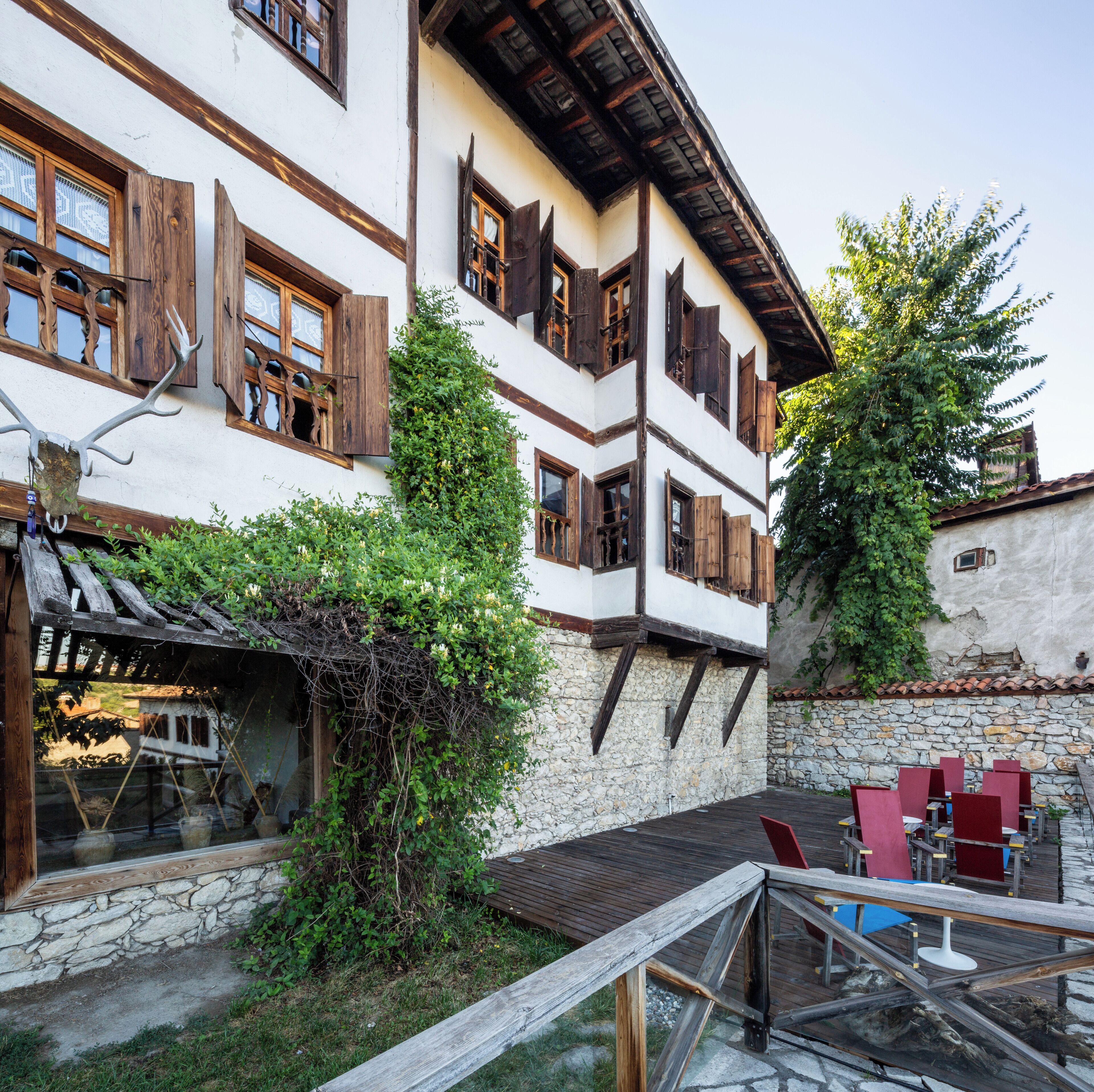 Ein traditionelles Gebäude mit steinernen Fundament, Holzbalken und einem Balkon mit roten Stühlen.