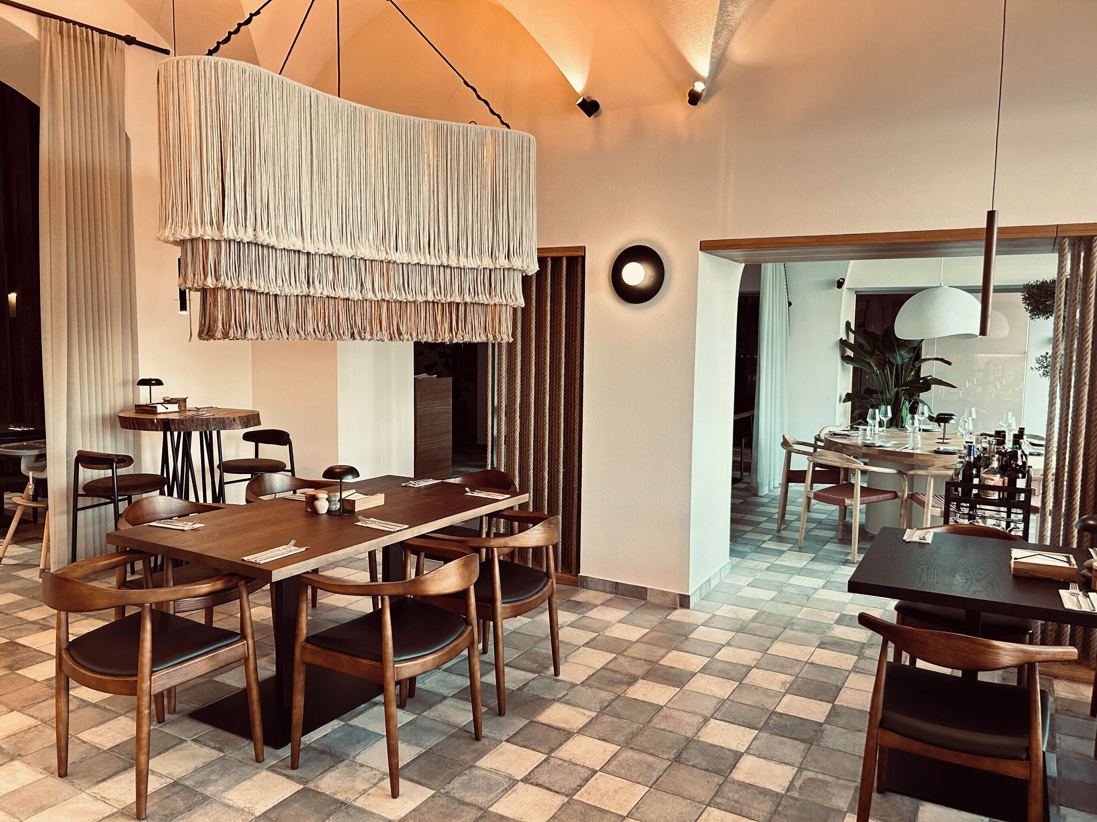 Un comedor con piso a cuadros, mesas y sillas de madera, y una lámpara colgante.