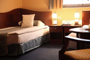 Quarto de hotel com cama, mesas de cabeceira, uma cadeira e janela.