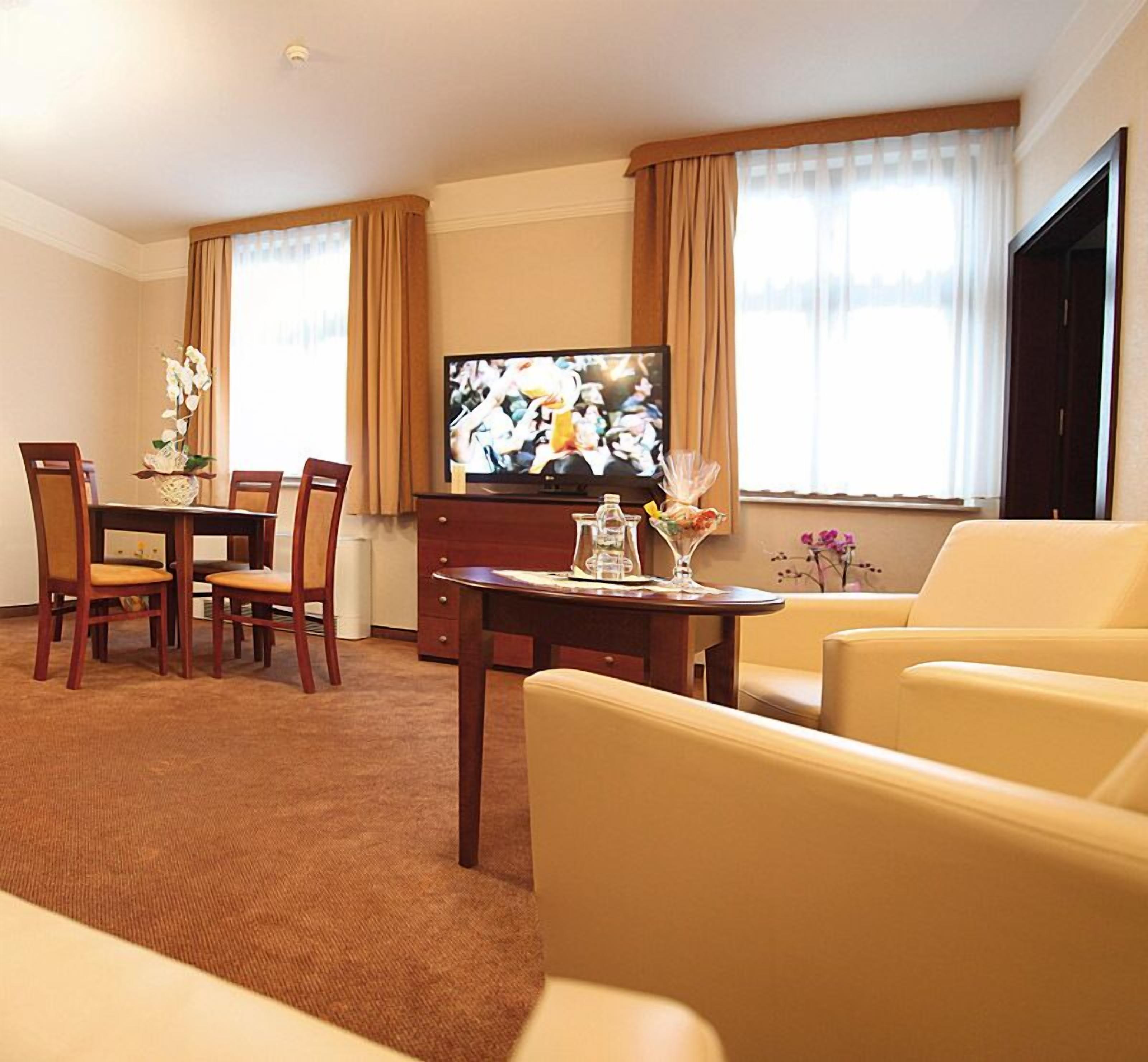 A hotel room with a dining area, a TV, and a sofa.