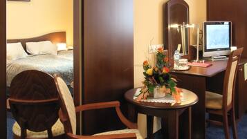 A hotel room with a bed, a desk with a computer, a chair, and a small table with a vase of flowers.