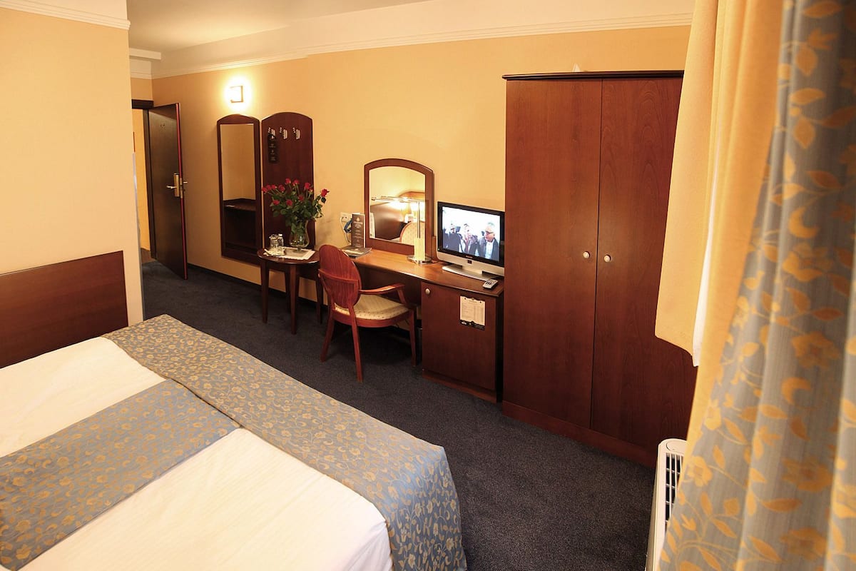 Quarto de hotel com cama, escrivaninha com computador, cadeira, guarda-roupa e espelho.
