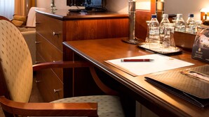 Une chambre d’hôtel avec un bureau en bois, une télévision, une lampe, un vase avec des fleurs et un plateau avec des bouteilles d’eau.