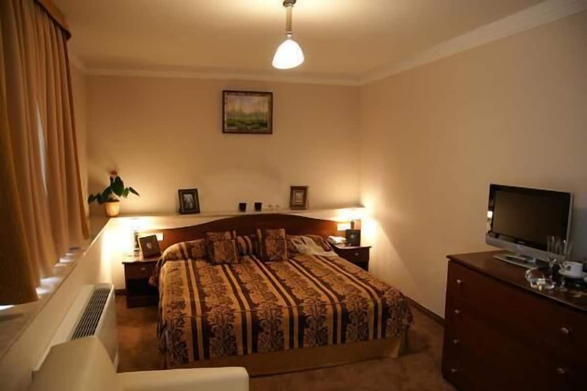 Quarto com uma cama grande, abajures, televisão e cômoda.