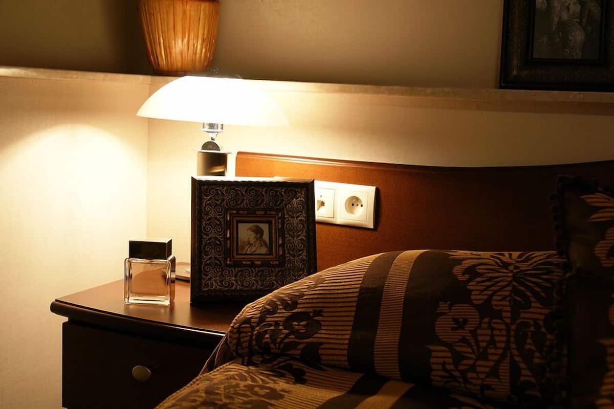 Quarto de hotel bem arrumado com mesa de cabeceira de madeira, abajur, quadro emoldurado e colcha estampada.