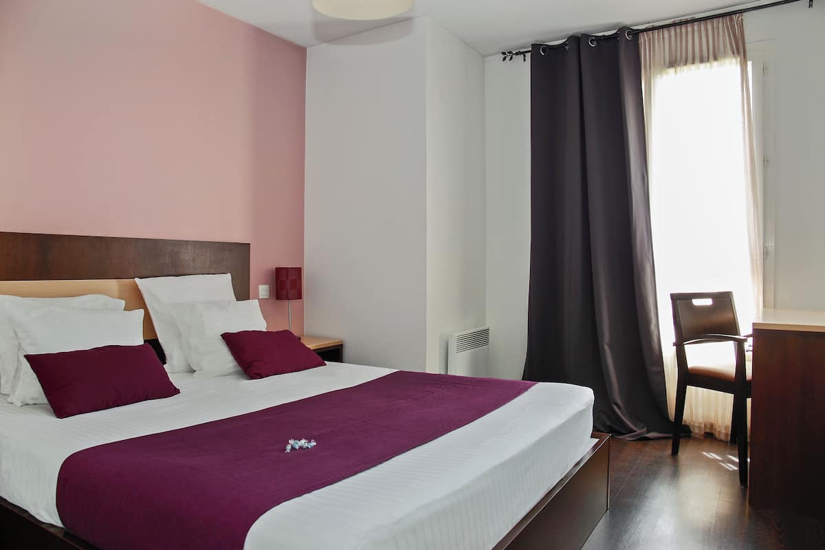 A hotel room with a bed, a desk, a chair, and a window with curtains.