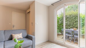 A modern living room with a grey sofa, a patterned pillow, a potted plant, and a dining area visible through a glass door. - Appart'City  Classic Toulouse Colomiers (Colomiers)