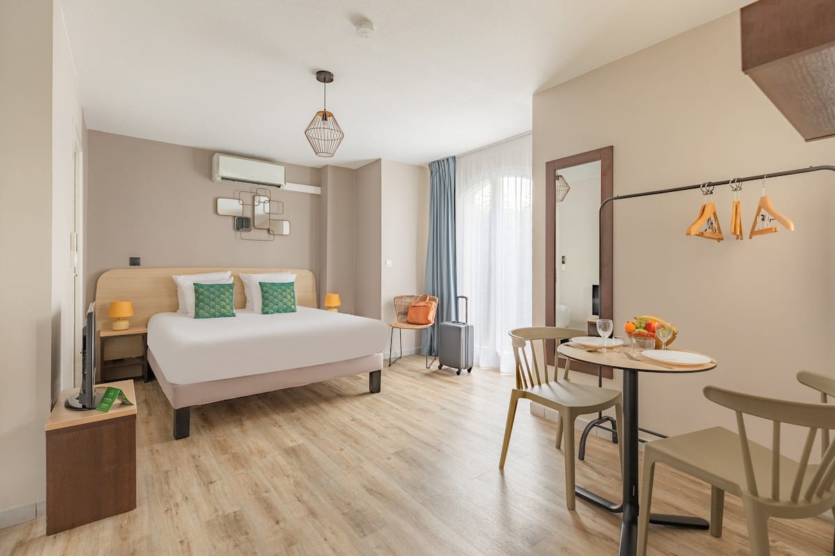 A hotel room with a bed, bedside tables, a desk with chairs, a mirror, and a window with curtains.