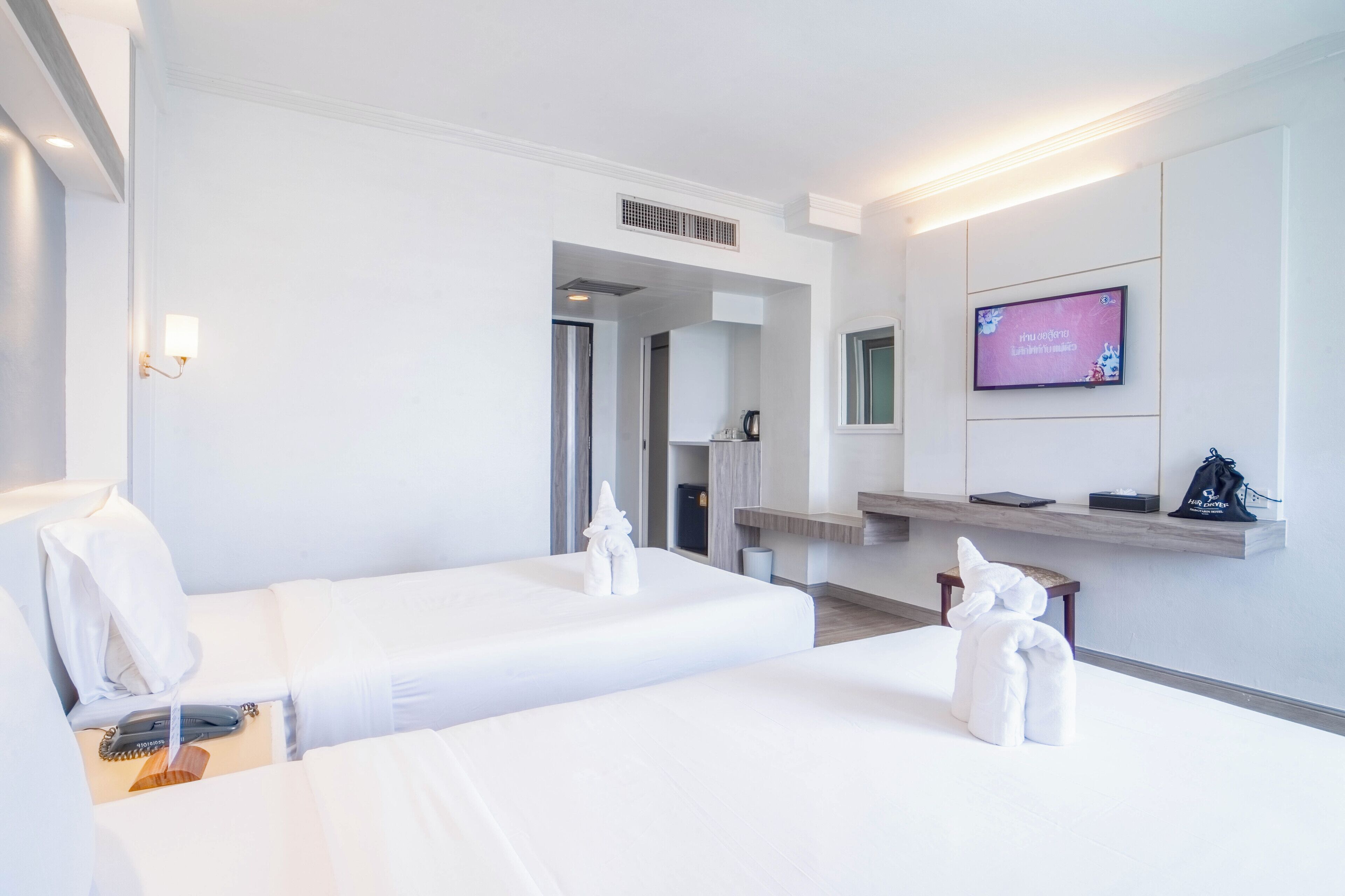 Ein Hotelzimmer mit zwei Betten, einem Fernseher, einem Schreibtisch und einem durchgegangenen Tür sichtbaren Badezimmer.