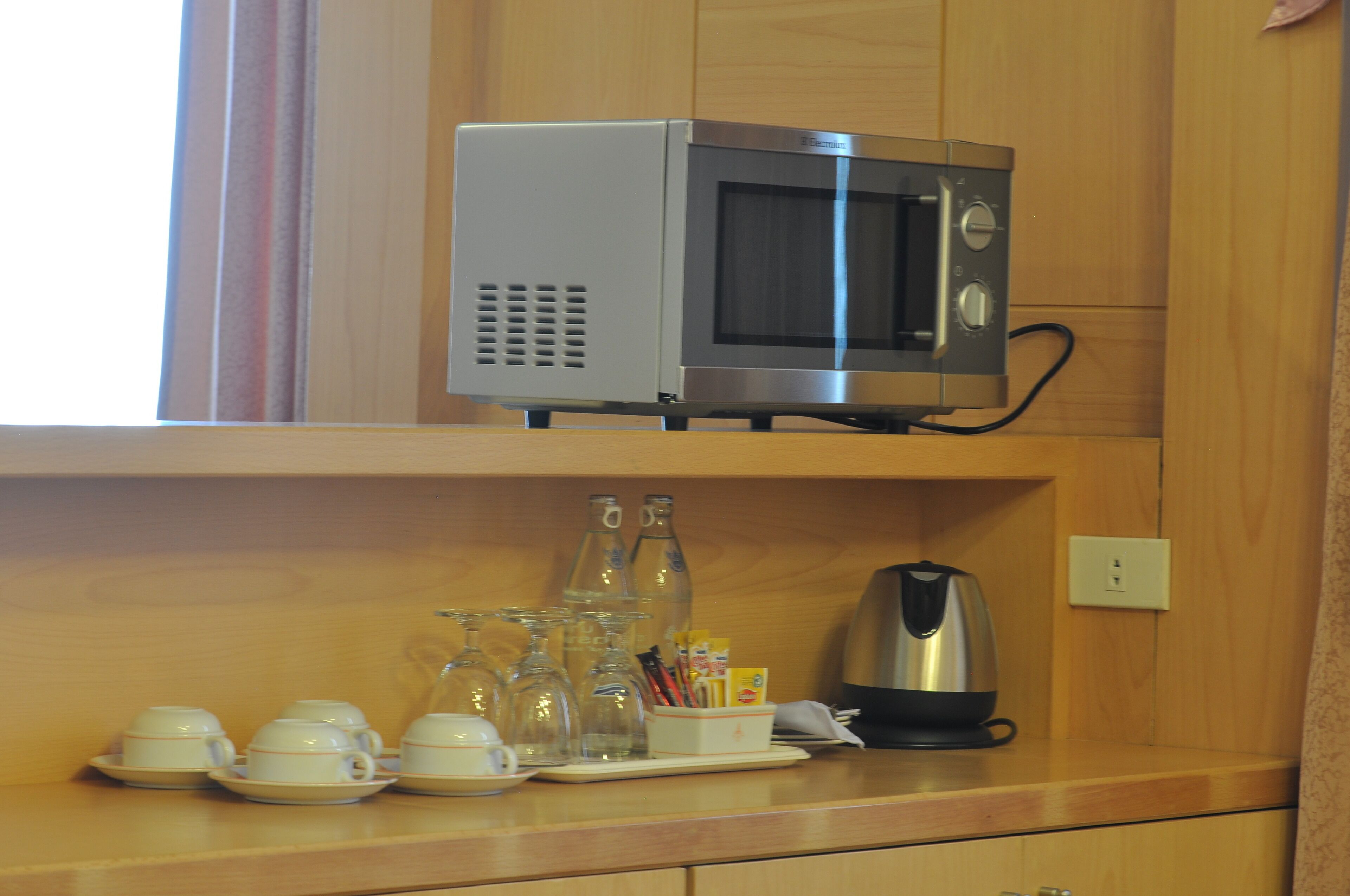 Une cuisine équipée d’un four à micro-ondes posé sur le plan de travail, d’une bouilloire et d’une étagère où sont rangées des tasses et des verres.