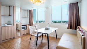 A modern living room with a dining area, a sofa, a chandelier, and large windows with curtains. - Thong Tarin Hotel (Surin)
