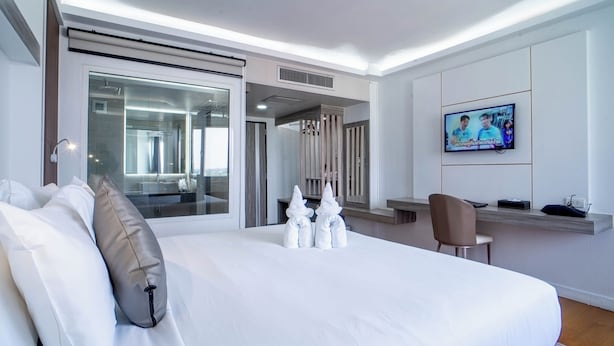 A modern hotel room with a large bed, a TV, a desk, and a view of the city. - Thong Tarin Hotel (Surin)
