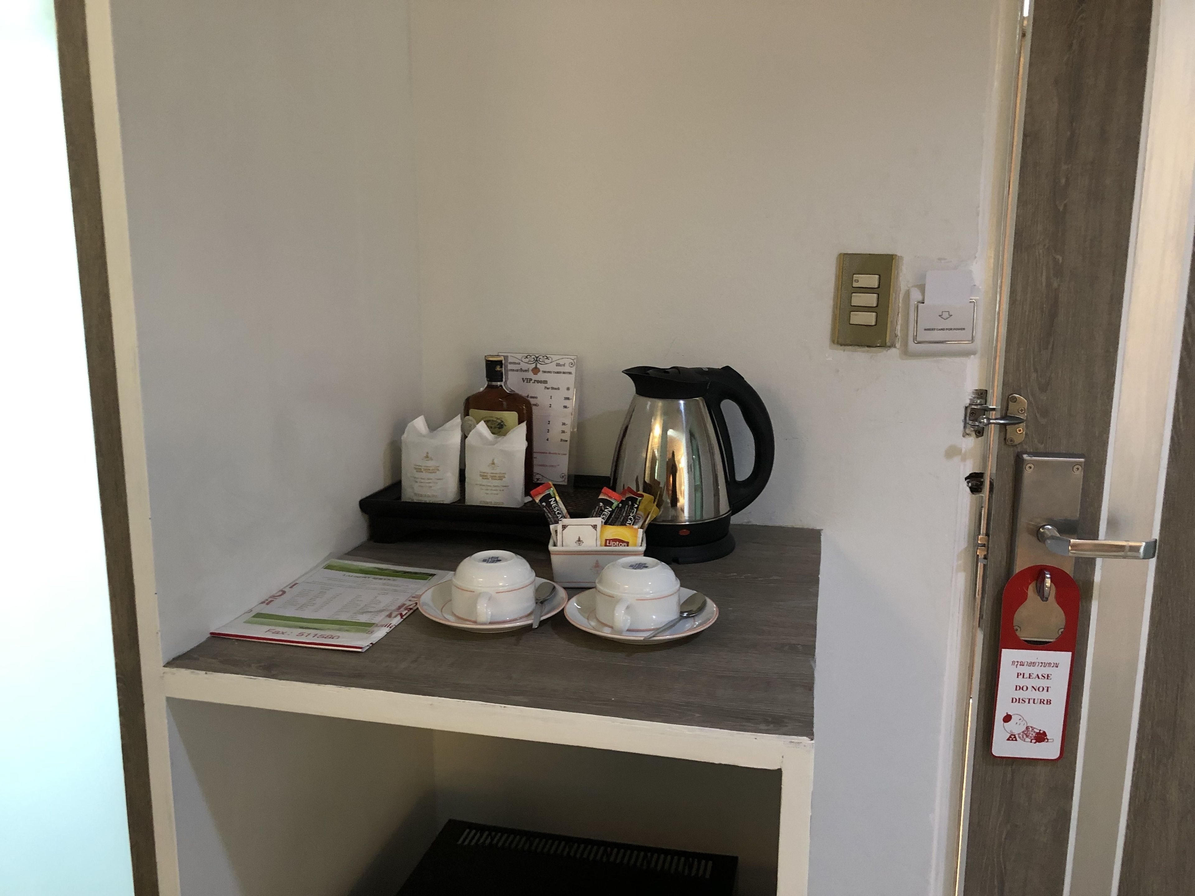 Una kitchenette pequeña con cafetera, bolsitas de té y tetera sobre una repisa.
