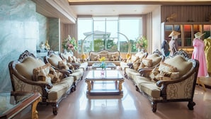 A luxurious living room with ornate furniture, a glass coffee table, and a large window offering a view of the city. - Thong Tarin Hotel (Surin)