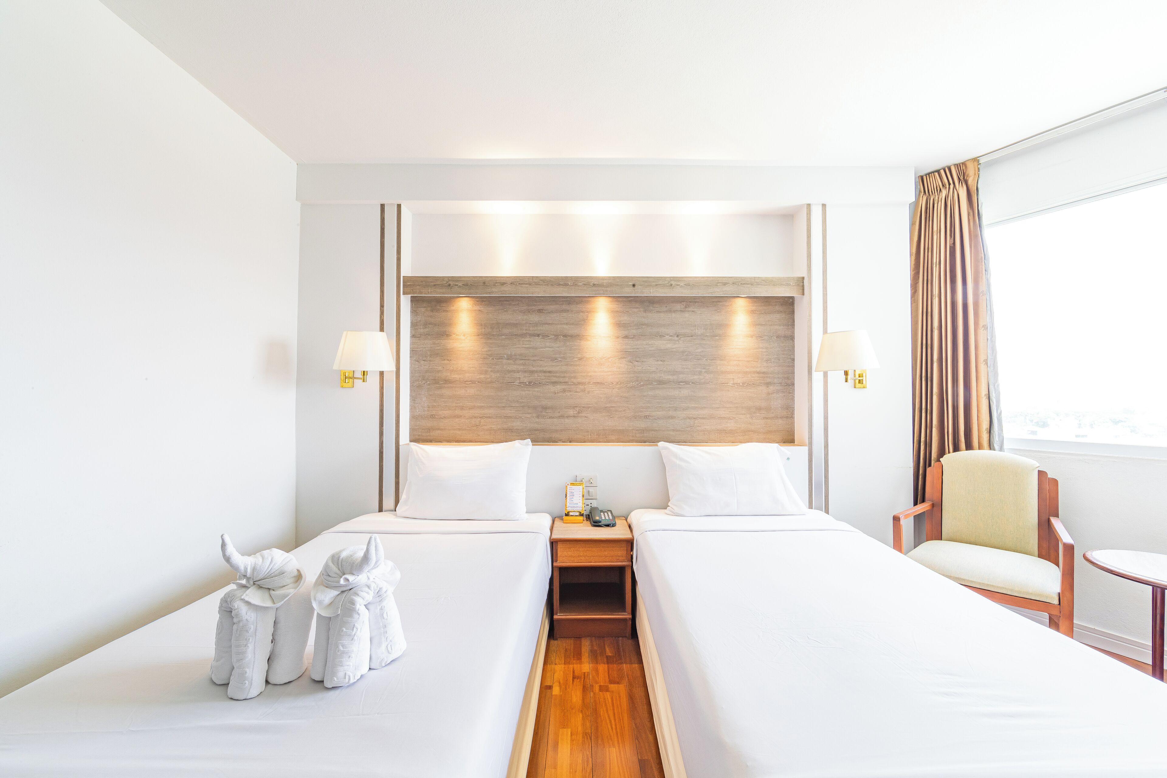 A hotel room with two beds, a wooden headboard, bedside lamps, a chair, and a small table.