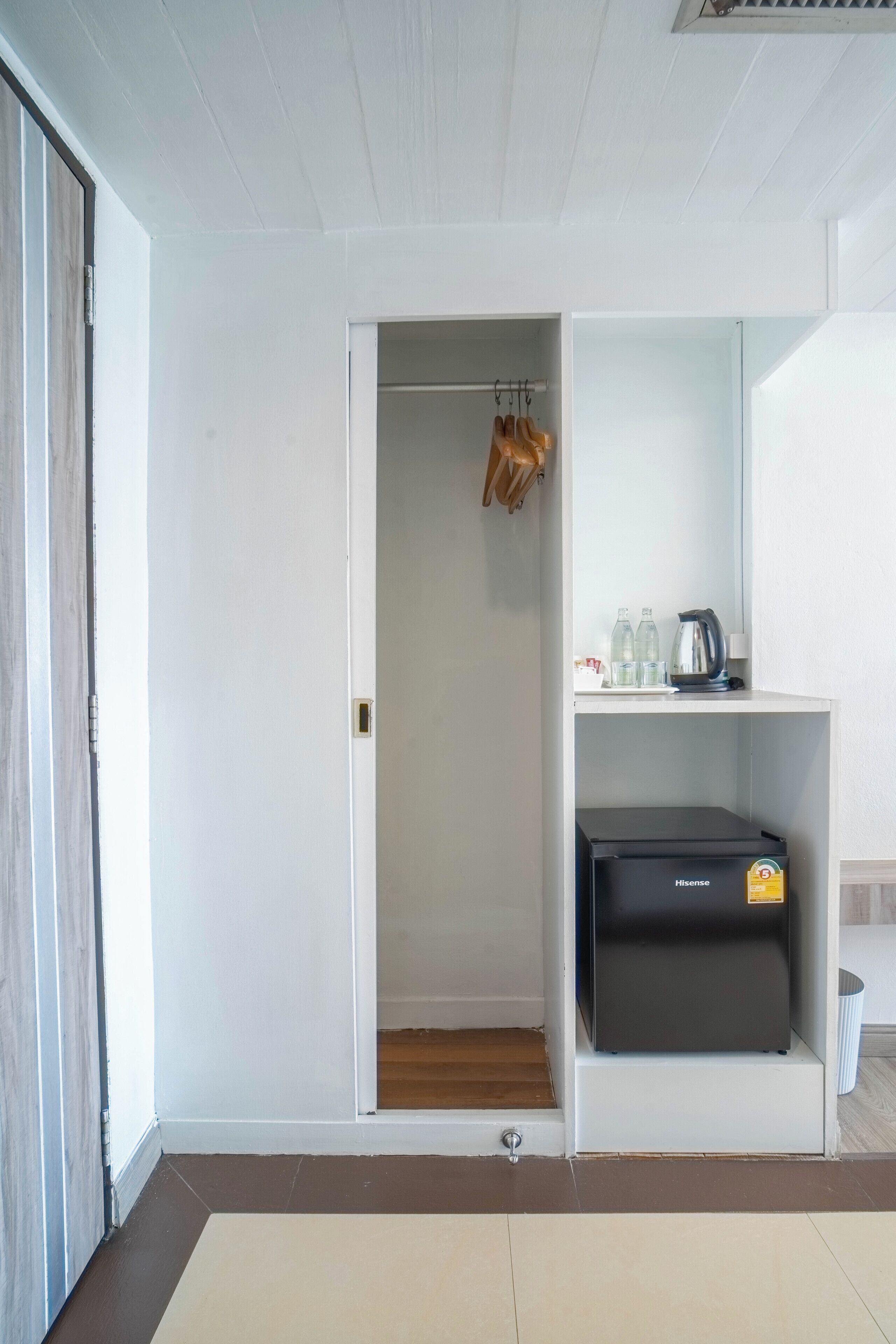 Een compacte kamer met een witte kast, een klein plankje met toiletartikelen en een zwart apparaat op de vloer.