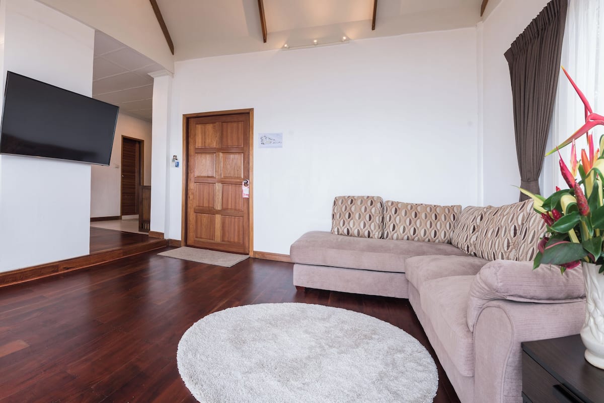 A modern hotel room with a wooden floor, a sofa, a TV, and a bed with a wooden headboard.