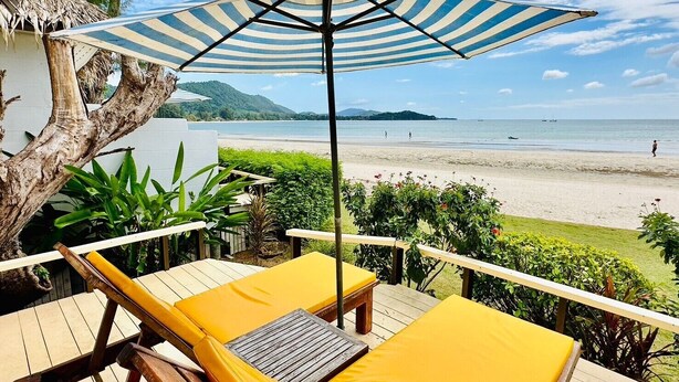 A deck with yellow lounge chairs and a striped umbrella overlooking a beach. - Twin Bay Resort (Ko Lanta)