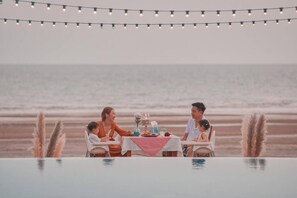 A dining table with a red and white checkered tablecloth, surrounded by chairs, set against a beach backdrop.