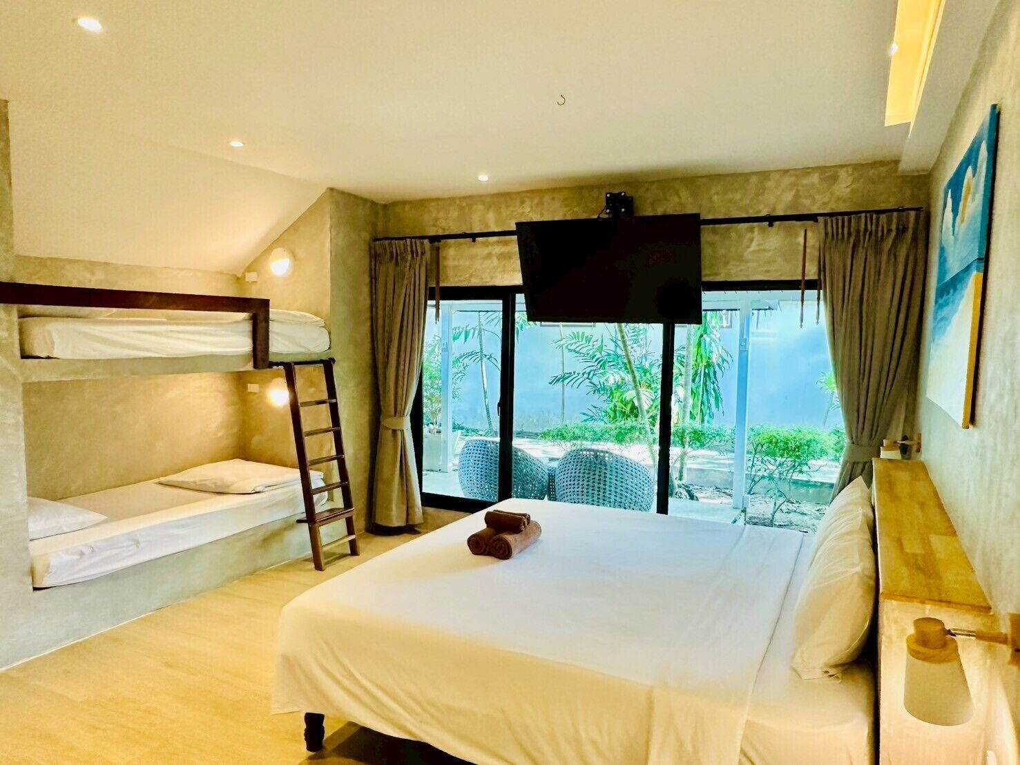 A hotel room with a bunk bed, a flat bed with a TV, and a balcony with outdoor seating.