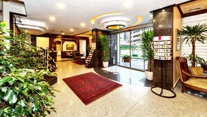 Un hall de hotel con alfombra roja, un mostrador de recepción, una zona de estar y una exhibición de revistas.