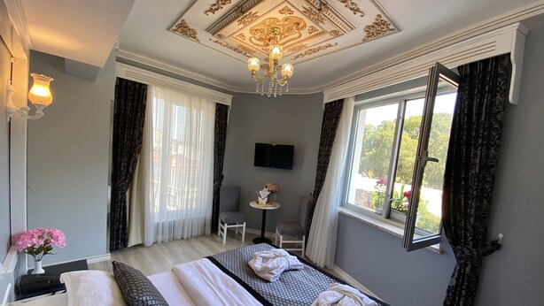 Habitación de hotel con una cama grande, una mesita, una silla, un televisor y una ventana con cortinas.
