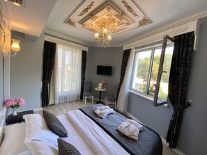 Habitación de hotel con una cama grande, una mesita, una silla, un televisor y una ventana con cortinas.