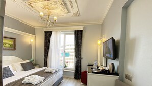 Habitación de hotel con cama, televisión, escritorio y una botella de agua, y vista al exterior.