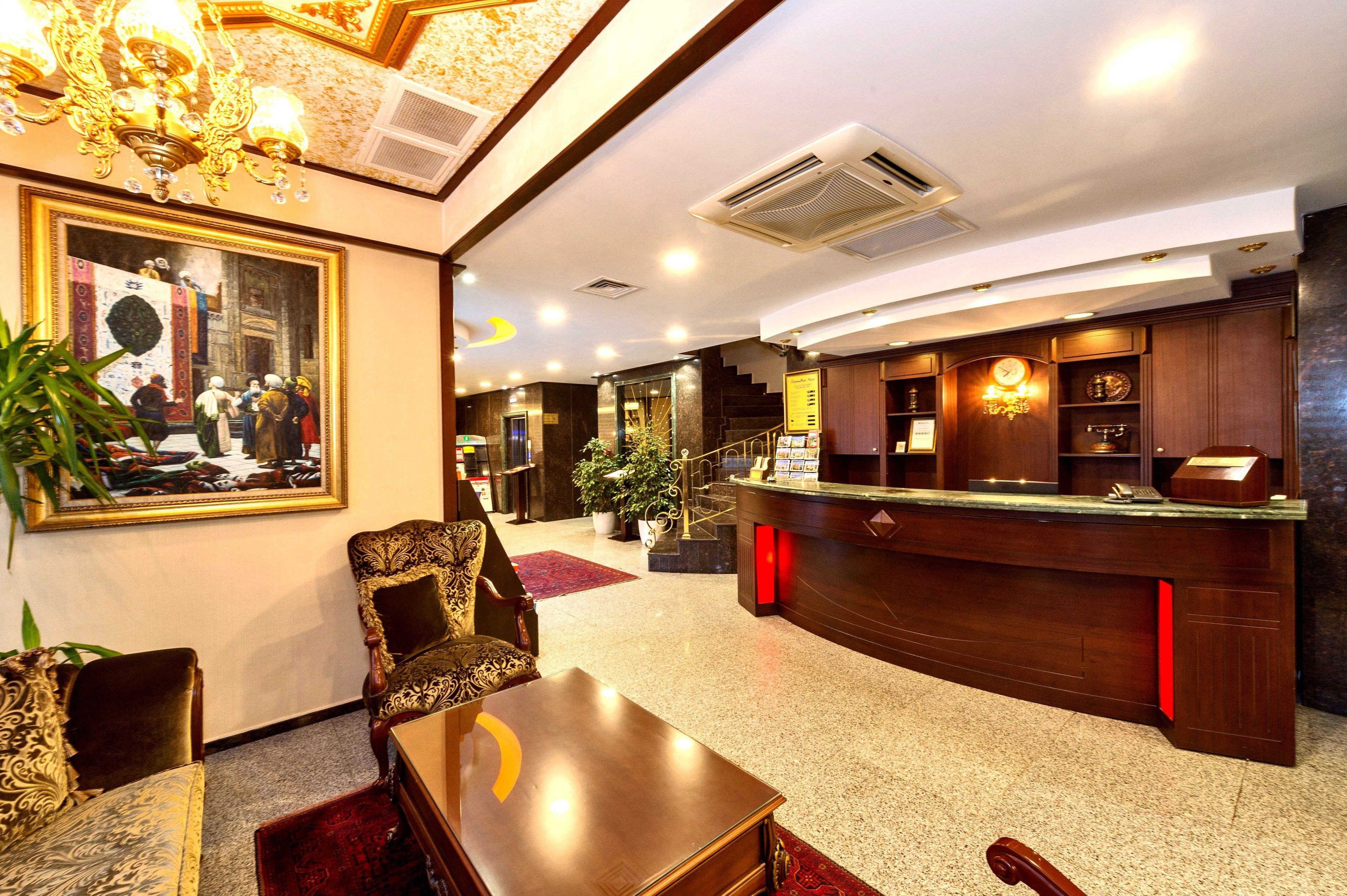 A lobby with a reception desk, a large framed painting, and a staircase leading to an upper floor.