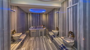 Un baño lujoso con piso de mármol, una bañera independiente y dos inodoros con detalles dorados.