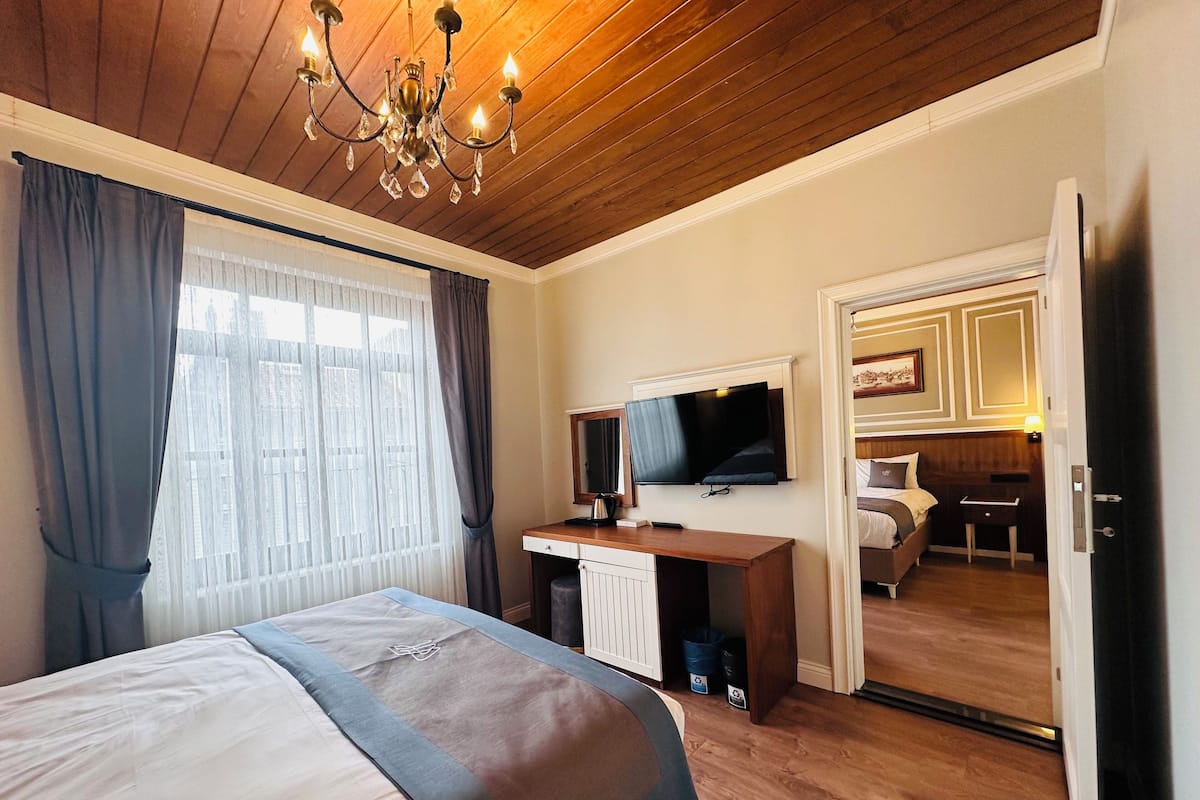 Habitación de hotel con cama, escritorio, televisor y puerta que da a otra habitación.