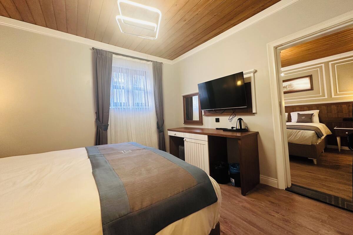 Una habitación de hotel con una cama, un escritorio con televisor, una ventana con cortinas y techo de madera.
