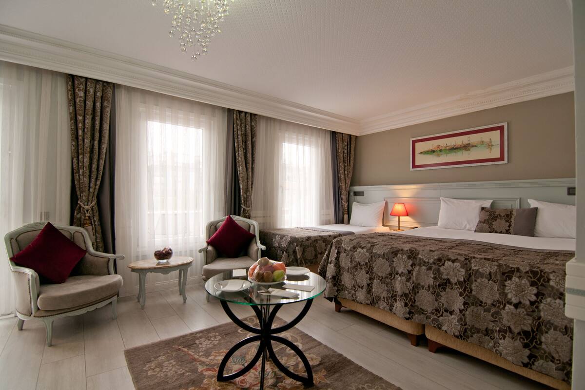 Habitación de hotel con cama, dos sillas, una mesita, lámpara y un cuadro en la pared.