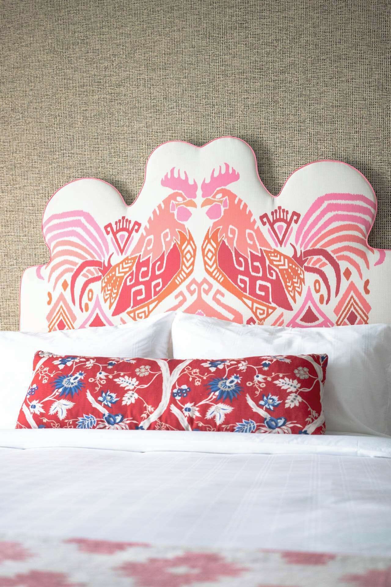 A bed with white linens, a red floral pillow, and a decorative headboard with a geometric pattern.