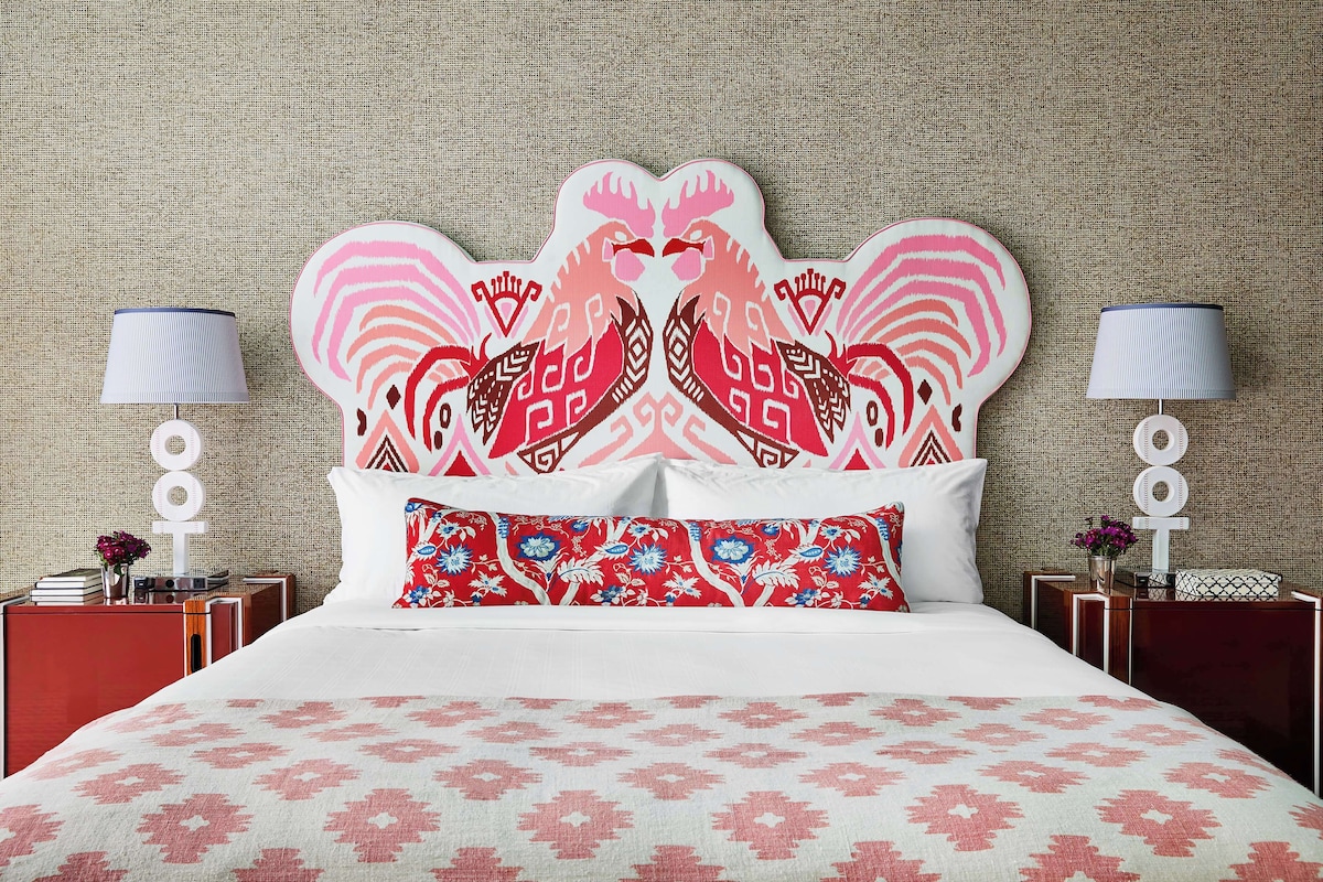 A bed with a patterned bedspread, a decorative headboard with a symmetrical design, two bedside tables with lamps, and a wall with a textured pattern.