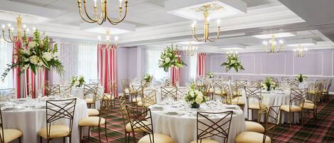 A banquet hall with round tables, gold chairs, and floral centerpieces.