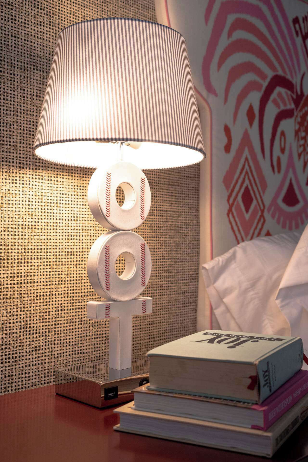 A lamp with a baseball design, a stack of books, and a patterned wall.