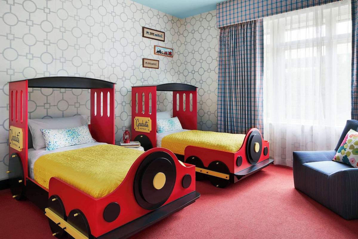 A children's room with two beds designed like trains, a red carpet, and a blue sofa.