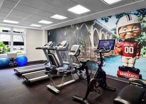 A gym with treadmills, elliptical machines, and a stationary bike. There is a large mural of a football player and a statue of a football player holding a ball.
