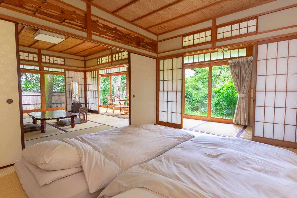 Ein traditioneller japanischer Raum mit Tatami-Böden, einer Futon-Liege, verschiebbaren Shoji-Türen und Blick ins Grüne.