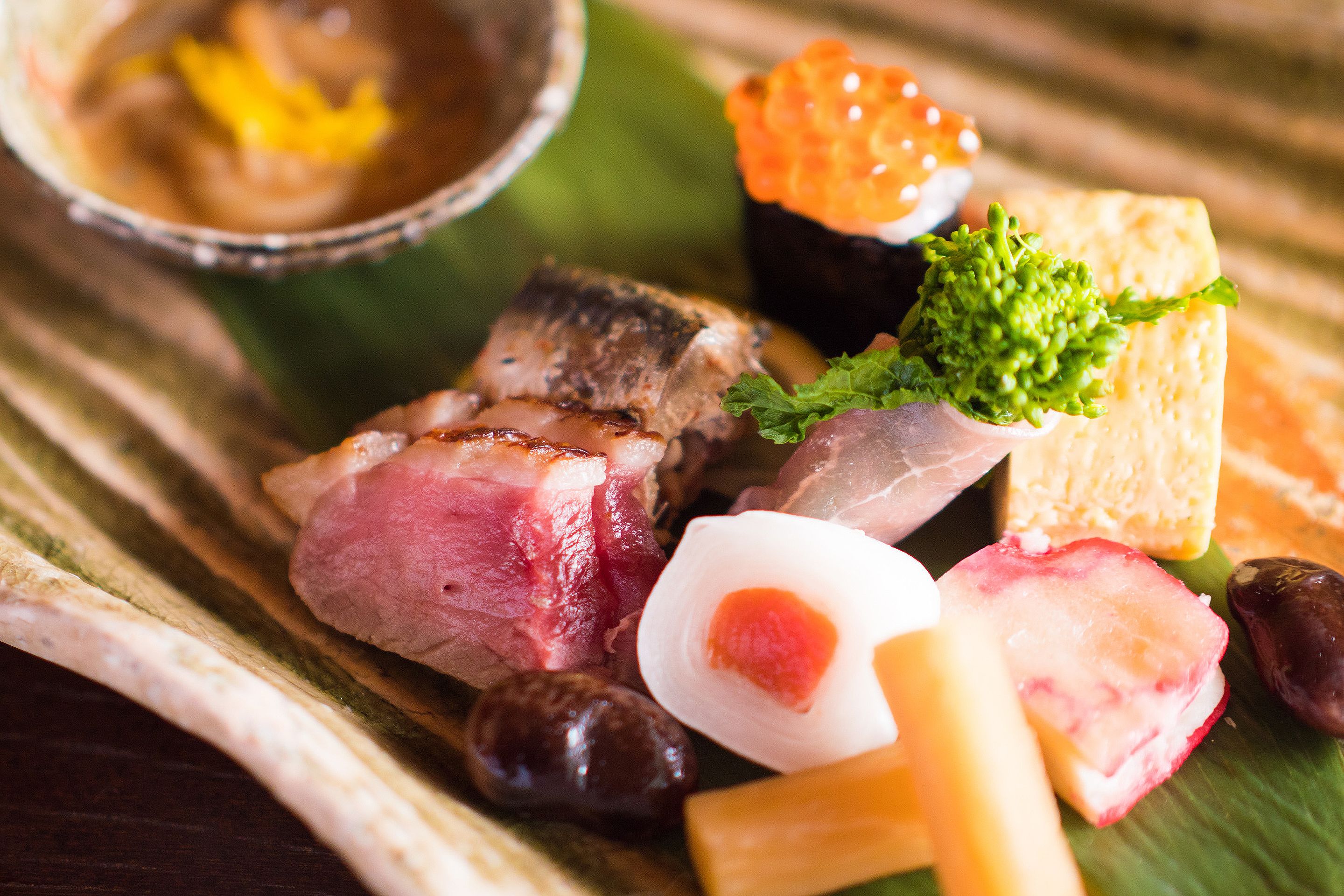 A variety of food items including sushi, meat, and vegetables on a wooden table.
