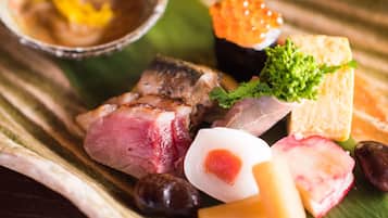 A variety of food items including sushi, meat, and vegetables on a wooden table.